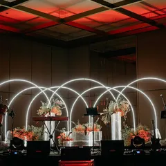 We designed this stunning stage for a live band performance at a reception, using intersecting neon arches and floral arrangements to create a vibrant and contemporary look.