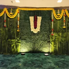 We create authentic South Indian themed decorations, perfect for a Roka ceremony. This backdrop uses a wall of fresh banana leaves, a faux grass panel, and marigold garlands for a traditional and natural feel.