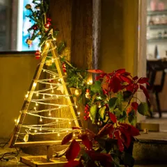We believe in sustainable celebrations. This close-up shows our alternative Christmas tree, crafted from wood and adorned with warm fairy lights and festive poinsettias.