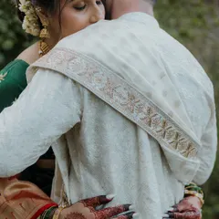 A close-up shot focusing on the details of a tender hug. The bride's henna-adorned hands and the intricate embroidery on the groom's shawl are beautifully highlighted.