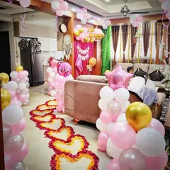 A lovely welcome home decoration for a baby. The setup features a pathway of hearts made from flower petals, balloon columns in pink and white, and a pink-themed backdrop in the living room.