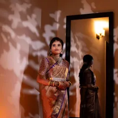 A creative shot of the bride's reception look. The warm lighting highlights her glowing skin and the beautiful details of her saree, while her reflection adds a touch of artistry.