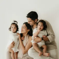 A classic family portrait with parents and their two daughters. The coordinated neutral outfits and simple background keep the focus on their connection.