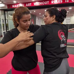 A coach demonstrates a grip-breaking technique with a student. Our women's BJJ sessions focus on practical skills that are effective regardless of size or strength.