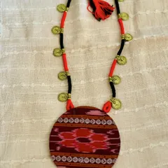 This pendant features a beautiful piece of Ikat fabric, known for its distinctive blurred patterns. I've paired it with a simple cord adorned with small metal coins to complement its tribal aesthetic.
