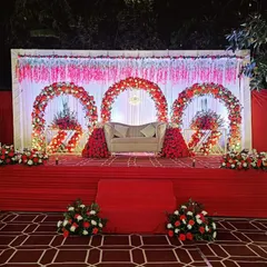 This magnificent stage is designed for a grand reception. It features three floral arches in red and white, a classic chaise lounge, and a cascading floral arrangement, all set against a backdrop of twinkling lights.