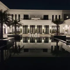 At night, the countryside farmhouse radiates a serene elegance. The pristine white facade is illuminated, reflecting beautifully in the dark water of the pool and highlighting the classical design elements that give the home its character.