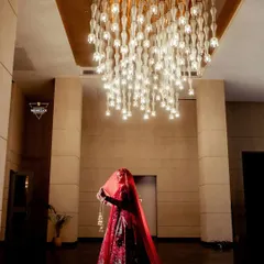 A dramatic silhouette of the bride holding her veil, standing under a magnificent modern chandelier. This shot is all about creating a grand and artistic bridal portrait.