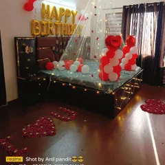 This is a complete birthday bedroom makeover. It features a lighted canopy, "HAPPY BIRTHDAY" foil balloons, and a personal touch with "I LOVE YOU" spelled out on the floor using rose petals.