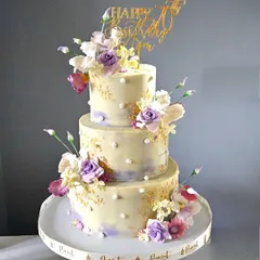 An elegant three-tiered cake to celebrate a 70th birthday. The cake has a subtle lavender and ivory watercolor finish, accented with gold leaf and beautiful, handcrafted sugar flowers.