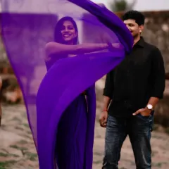 A playful, happy moment. The vibrant purple fabric of the flying saree creates a beautiful frame as it dances in the wind.