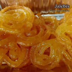 A close-up of our curvy and delicious Jalebis. You can see the syrupy glaze on each spiral. We make them fresh so you can enjoy them warm and crispy.