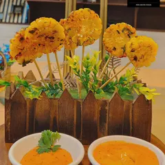 A playful and creative appetizer, these corn lollipops are a visual delight. Spiced corn patties are served on sticks and arranged like a floral bouquet, complete with dipping sauces, making them a fun and delicious starter.
