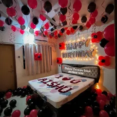 A romantic red and black themed birthday room decoration. The setup includes balloons on the ceiling and floor, and a personalized message on the bed.