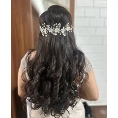 A perfect hairstyle for a reception or engagement. This is a classic half-up style with voluminous, bouncy curls and a delicate floral hair accessory that adds a touch of modern elegance.