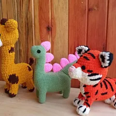 A trio of colorful animal friends: a yellow giraffe, a green dinosaur with pink plates, and a bright orange tiger.