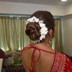 A clean and classic bridal bun wrapped in a string of fresh white flowers (gajra). This traditional hairstyle is elegant and perfectly complements a red lehenga.
