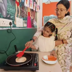 An instructor guides a student as she learns to flip a pancake on an induction cooktop. We prioritize safety and hands-on learning, ensuring each child gains confidence in the kitchen.