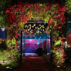 A floral archway of red and green botanicals creates a vibrant transition into the main event space, offering a glimpse of the dazzling party inside.