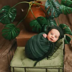 This nature-inspired newborn shoot uses rich green tones and botanical elements. The baby is safely swaddled on a miniature bed, creating a beautiful contrast that makes their delicate features stand out.