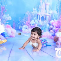 A smiling baby mermaid explores her underwater kingdom, complete with a rocking seahorse and a unicorn plush. The pastel colors and castle backdrop create a whimsical and enchanting scene.