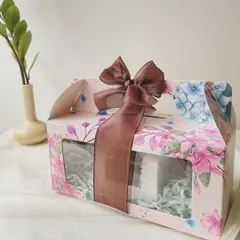 The Rakhi Celebration Hamper, presented in a beautiful floral box with a brown ribbon. This gift set includes our popular choco almonds, wheat double chocolate cookies, rich brownies, and our signature Regal Riches.
