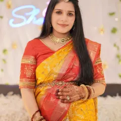 A radiant solo portrait of the mother-to-be at her baby shower. She is dressed in a stunning yellow and red saree, with beautiful henna on her hands, surrounded by festive decorations.