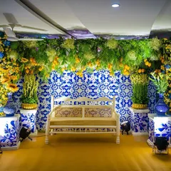 A unique Mehendi seating area with a backdrop of blue and white Portuguese-style tiles. The vibrant yellow and blue floral arrangements create a stunning contrast, perfect for a themed celebration.