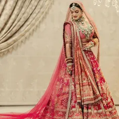 A full-length portrait of the bride in a magnificent pink and red lehenga, its long train spread out, showcasing the grandeur of her bridal look.