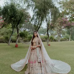 A full-length portrait of the bride in a magnificent lehenga with a long, flowing train. Set against a natural green backdrop, this image is the epitome of bridal elegance and grace.