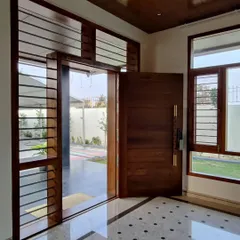 A large, solid wood pivot door serves as a grand entrance. The combination of wood and glass with clean lines creates a modern yet warm welcome.