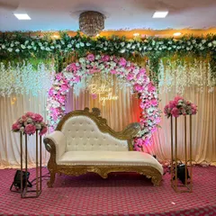 For an elegant engagement, anniversary, or pre-wedding party, we design stunning stage setups. This one features a beautiful floral ring with a 'Better Together' neon sign, complemented by a classic chaise lounge and matching flower stands, creating a sophisticated focal point in a banquet hall.