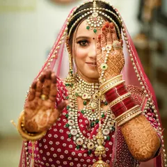 A playful and classic bridal pose. The bride peeks through her hands, showcasing her intricate mehndi design and her sparkling eyes, a perfect blend of tradition and personality.