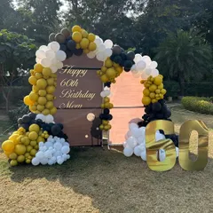 An elegant outdoor 60th birthday celebration for a client's mom. The setup features a custom backdrop with a beautiful balloon arch in mustard yellow, black, and white.