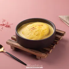 This Rasmalai shot uses a modern, minimalist setup with a pink background to make the traditional sweet feel contemporary. The focus is on the creamy texture and the vibrant yellow color from the saffron.
