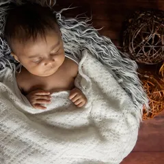 Here, I used a soft white blanket to gently wrap the baby, creating a sense of security. The dark, textured background provides a beautiful contrast, making the peaceful newborn the central focus.