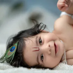 A playful and charming portrait of a baby boy dressed as Krishna. His sweet, curious expression and the peacock feather in his hair make this an unforgettable shot.