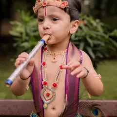 This adorable little boy, dressed as Krishna, pretends to play a flute. Themed shoots like this allow for fun, interactive, and memorable child photography.