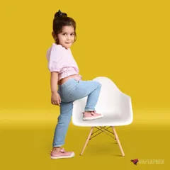 A fun and playful full-body shot of a child interacting with a chair. The bright yellow backdrop and the child's energetic pose capture the joyful spirit of childhood.
