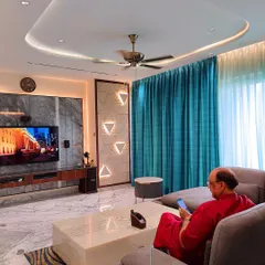 A client enjoying their new living room. The space features a monochromatic palette with grey-veined Statuario marble, a comfortable sofa, and a custom TV unit, all designed for relaxation and timeless appeal.