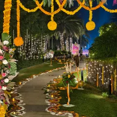 A stunning entrance and walkway for a large-scale outdoor Diwali party. We used extensive flower rangoli, hanging marigold garlands, and warm fairy lights to create a grand and welcoming path for guests.