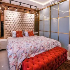 I believe a bedroom should be a personal sanctuary. For this master bedroom, I designed a floor-to-ceiling tufted headboard to create a sense of luxury, paired with a vibrant red ottoman for contrast. The lacquered glass wardrobe with gold accents adds a touch of glamour and provides ample storage.