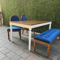 A classic dining set with a twist. It features a teak table with a white-painted base, two royal blue upholstered chairs, and a matching tufted bench for flexible seating.