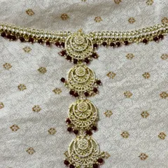 This rental hair choti features chandbali-style motifs with red bead drops. It's the perfect finishing touch for a bridal hairstyle.