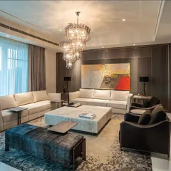 A spacious and open living room where comfort is key. The furniture arrangement includes multiple sofas and armchairs in neutral tones, creating an inviting atmosphere for large gatherings. The design emphasizes clean lines and high-quality materials to achieve a look of timeless elegance.