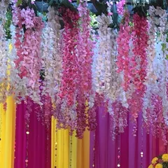 Details make the decor. This close-up shows the beautiful texture of hanging floral strings against a backdrop of colorful yellow and pink drapes, perfect for creating a festive photo booth or entrance for any celebration.