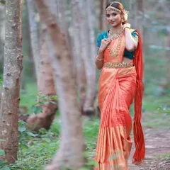 A full-length portrait in a serene, wooded location. The way the orange silk saree stands out against the natural background makes for a stunning and timeless image.