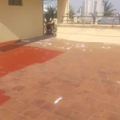 This image captures the waterproofing application in progress. You can see the original terracotta tiles being covered by the new protective red coating, demonstrating the transformation and coverage achieved.