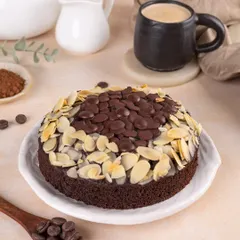 The full chocolate almond cake, ready to be served with coffee, showcasing its rich topping of chocolate chips and sliced almonds.