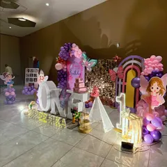 A wide view of a butterfly and fairy-themed first birthday party. This setup includes a shimmering sequin backdrop, large 'ONE' letters for photos, and custom fairy and butterfly cutouts, all tied together with a purple and pink balloon garland.
